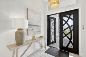 Professional wide-angle exterior photo of a gray modern home in Cape Coral Florida with a paved driveway, palm trees, and bright blue sky.