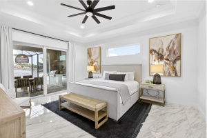 Professional interior photo of a luxury master bedroom featuring a king bed, tray ceiling with fan, and large sliding glass doors leading to a pool area. Done by Realty Media 360 in Cape Coral Florida.