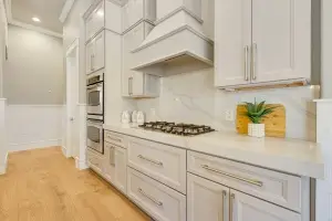 Close-up interior photography by Realty Media 360 of a modern white kitchen featuring custom shaker-style cabinets, a professional range hood, and sleek stainless steel ovens in Englewood Florida..