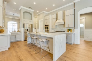Professional interior photography by Realty Media 360 of a modern white kitchen featuring a large marble waterfall island, gold hardware, and stainless steel appliances.